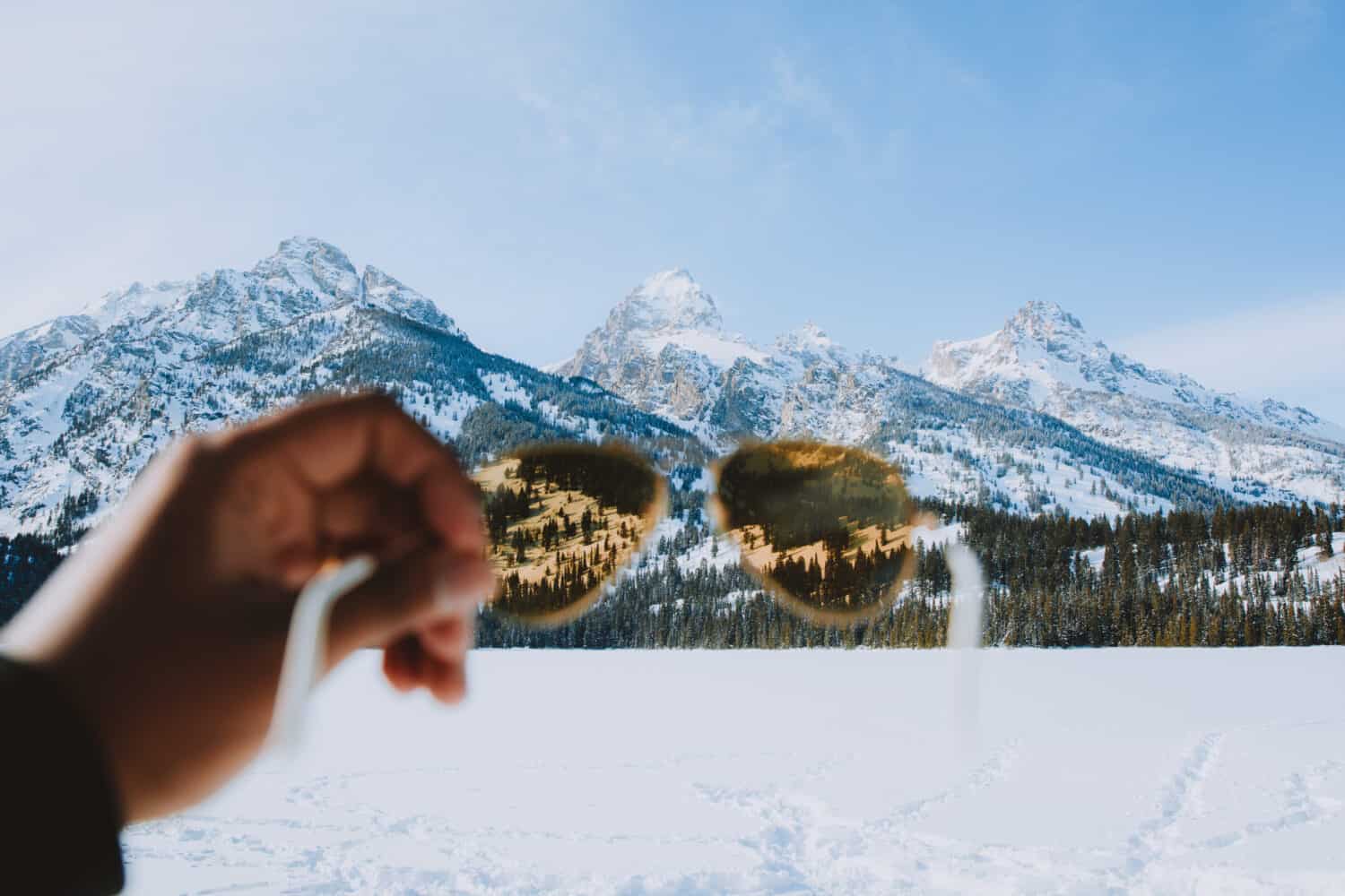 Berty Mandagie holding up polarized sunglasses un Wyoming in winter - TheMandagies.com