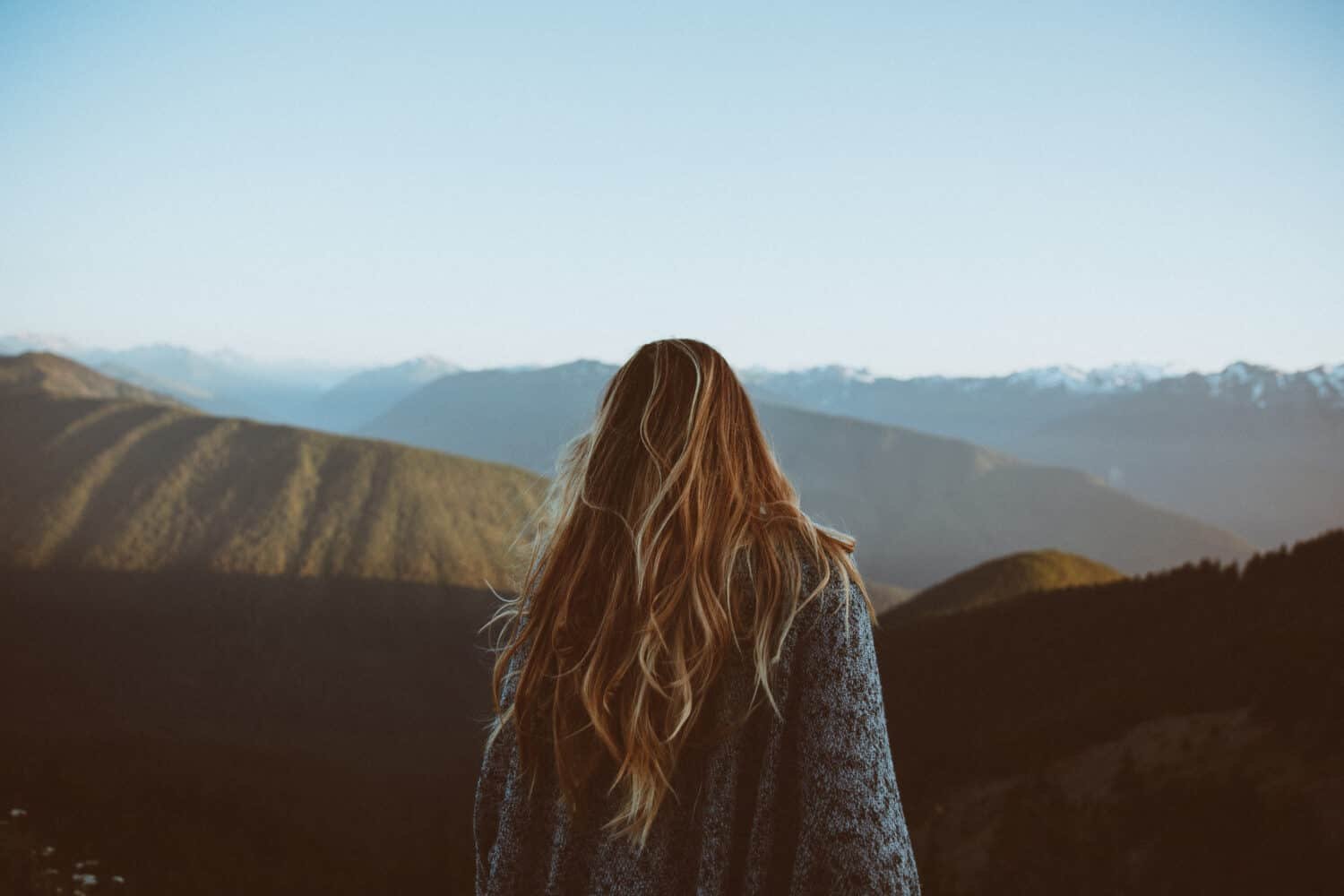 Emily Mandagie standing and lookout out at the landscape of green rolling hills during sunset at Hurricane Ridge in Olympic National Park