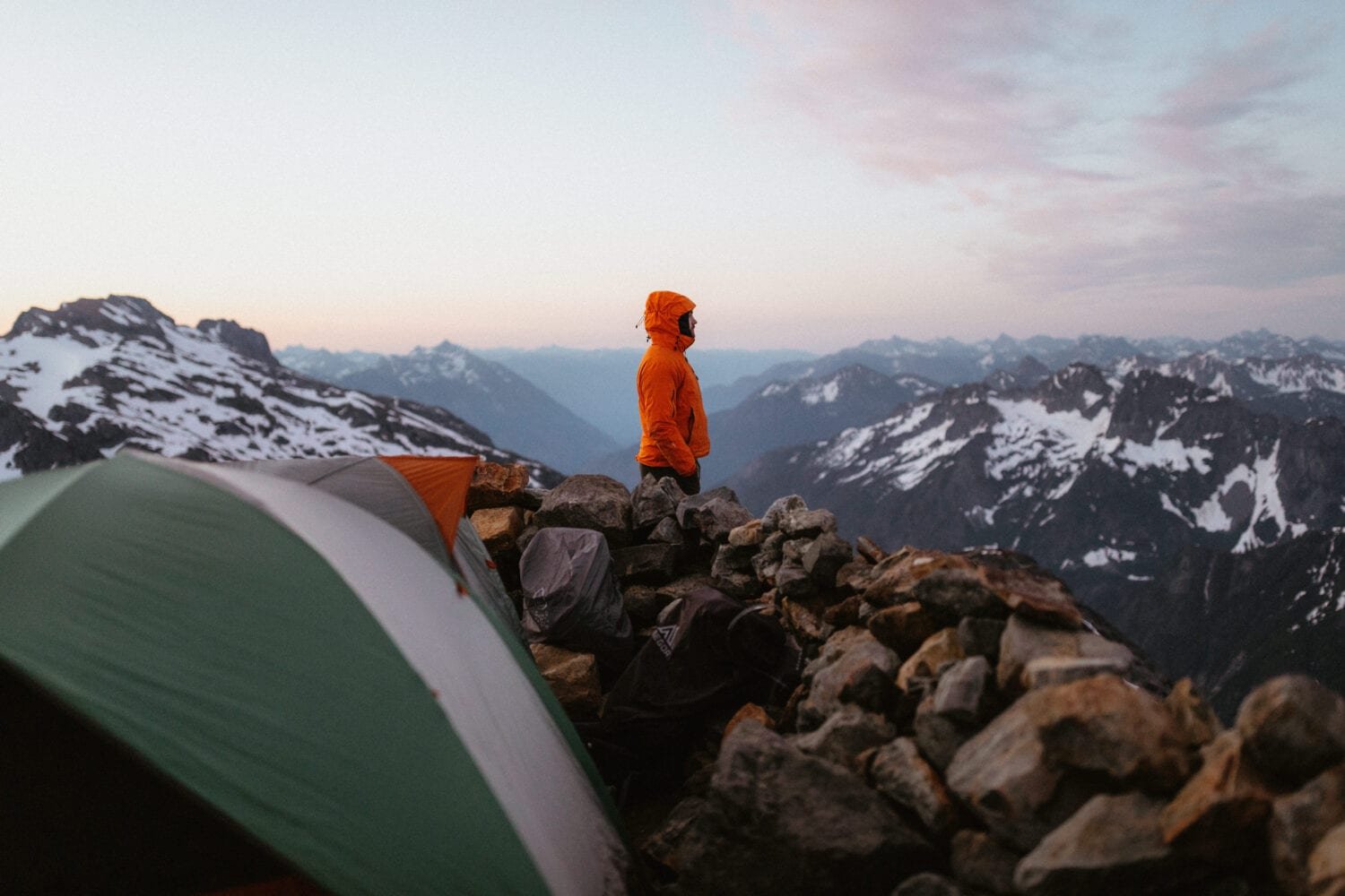 Man in orange jacket looking at the North Cascade Mountain Range in Washington during sunset.