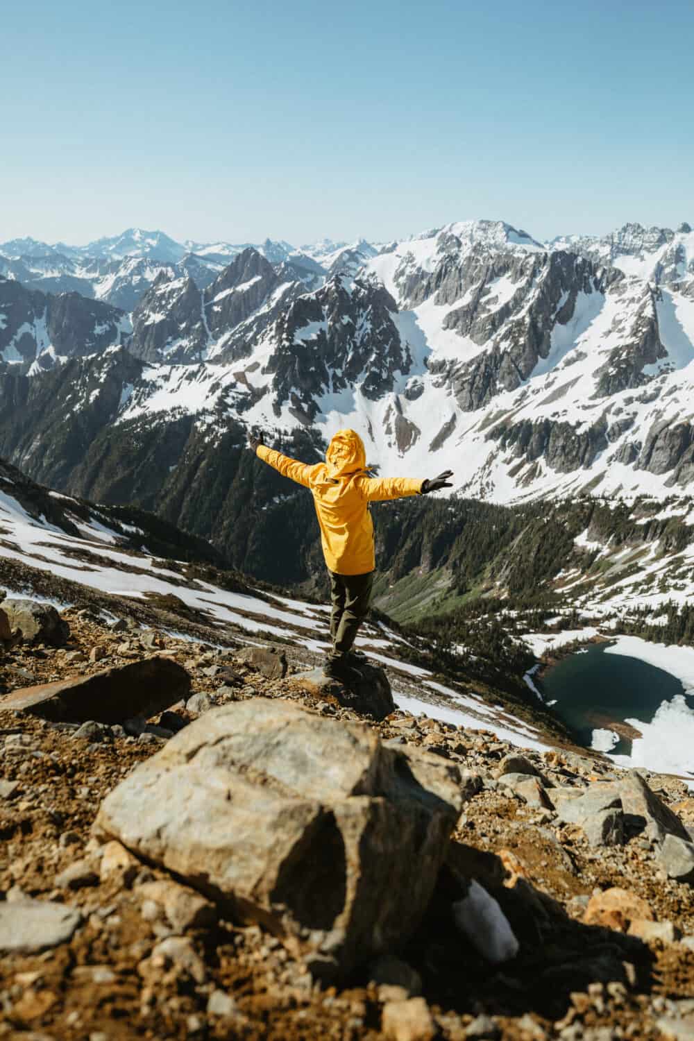 Man in yellow jacket, standing in front of North Cascade Mountain range in July