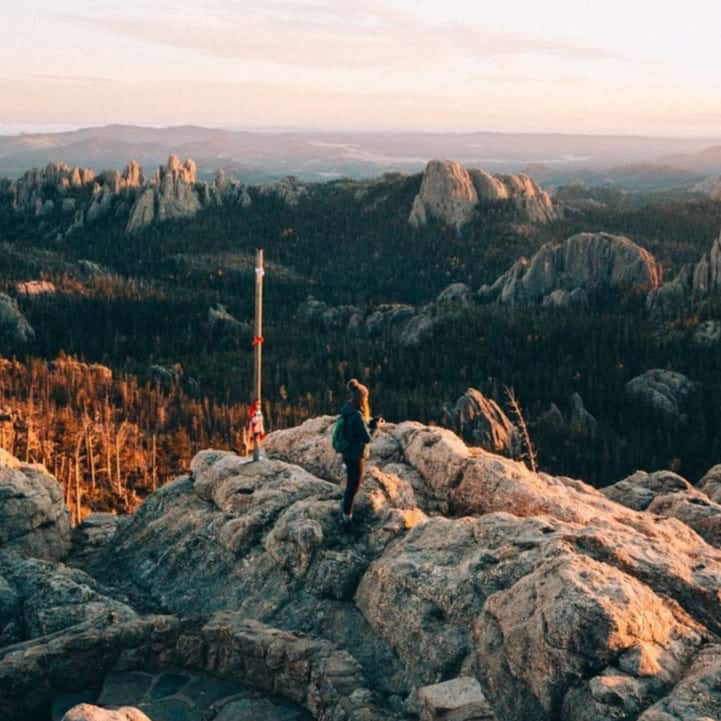 A mountain vista captured from above by drone, with a woman standing on a peak.
